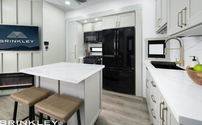 | Model Gx Toy Hauler Line 73 A spacious RV kitchen in the Brinkley Model Gx, showcasing hardwood trim, integrated LED lighting, and high-end residential-style hardware and finishes.