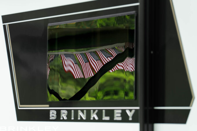 | Model Z AIR Travel Trailer Line 64 Luxury Travel Trailer Modern Square Frameless Windows with reflection of US flags at a campground during 4th of July.